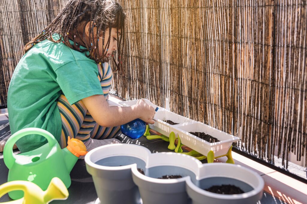 kid at the balcony watering plants with a spray