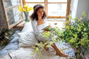 Pretty african american girl reading book sitting on windowsill