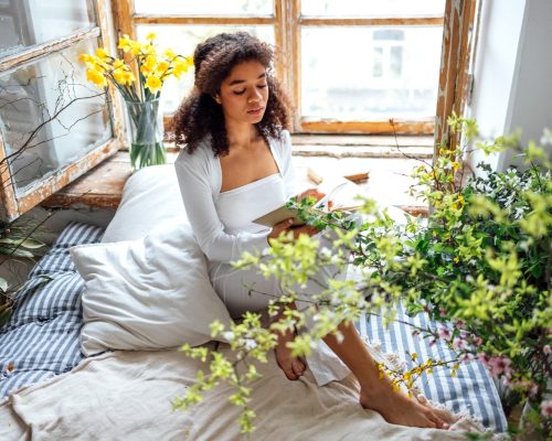 Pretty african american girl reading book sitting on windowsill